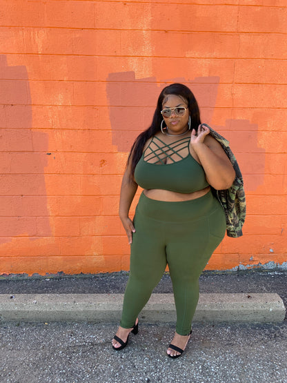 A person wearing green leggings with two side pockets, standing in front of an orange wall.
