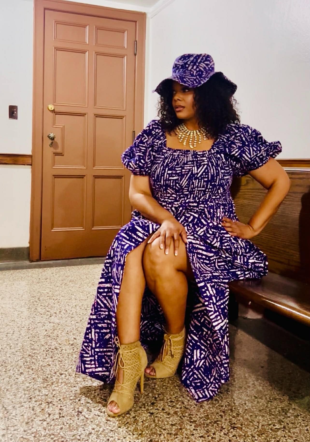 Woman in a purple and white patterned dress sitting on a bench indoors.
