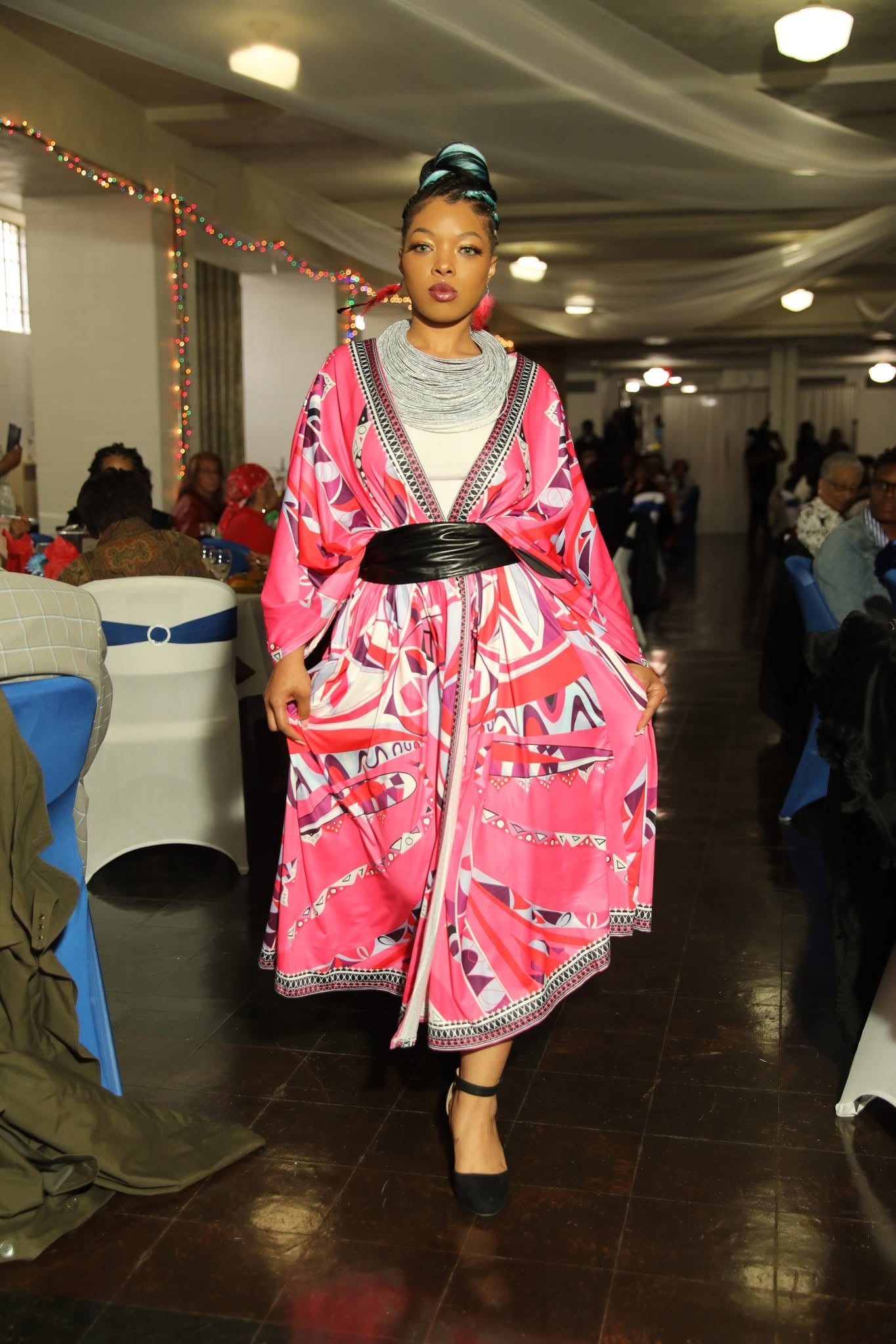 Woman in a pink dress with patterns walking in an indoor setting.