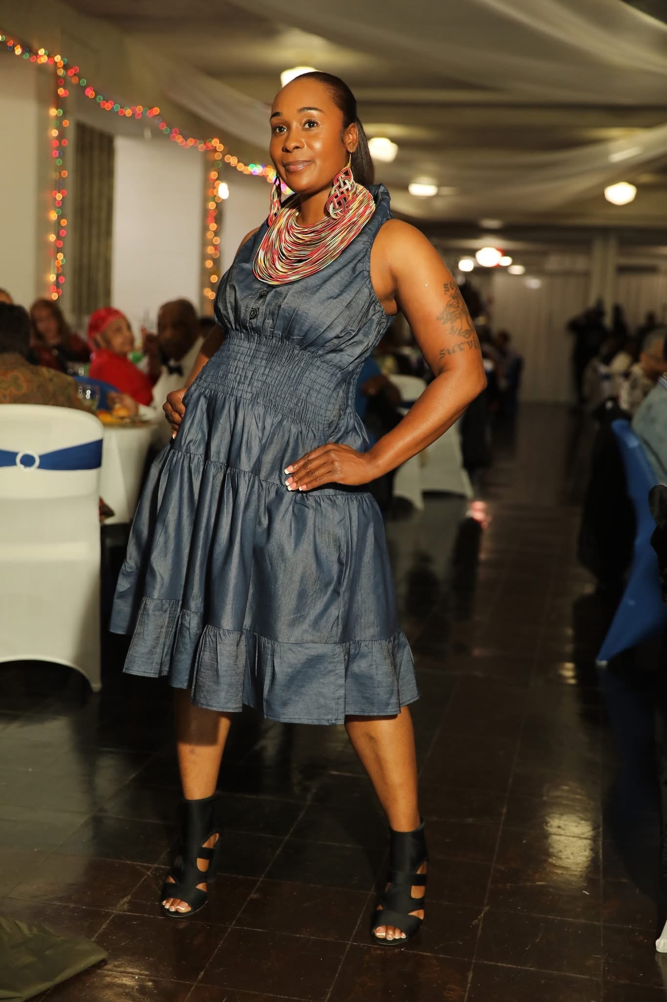 Woman in a blue dress standing in a room with tables and people in the background