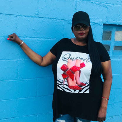 A person wearing a black tunic tee shirt with a graphic, blue ripped jeans, and red sneakers standing in front of a blue wall.